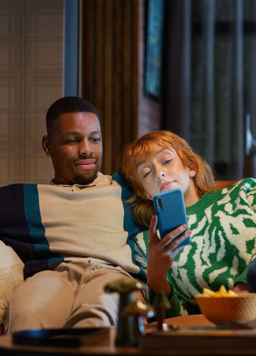 Eine Frau und ein Mann sitzen auf dem Sofa und blicken in ein Smartphone