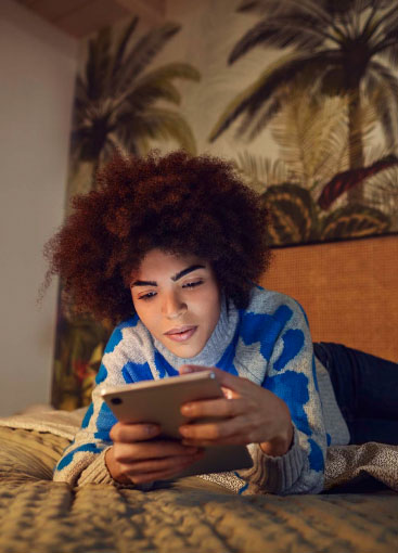 Eine Frau liegt auf dem Bett und schaut aufs Tablet