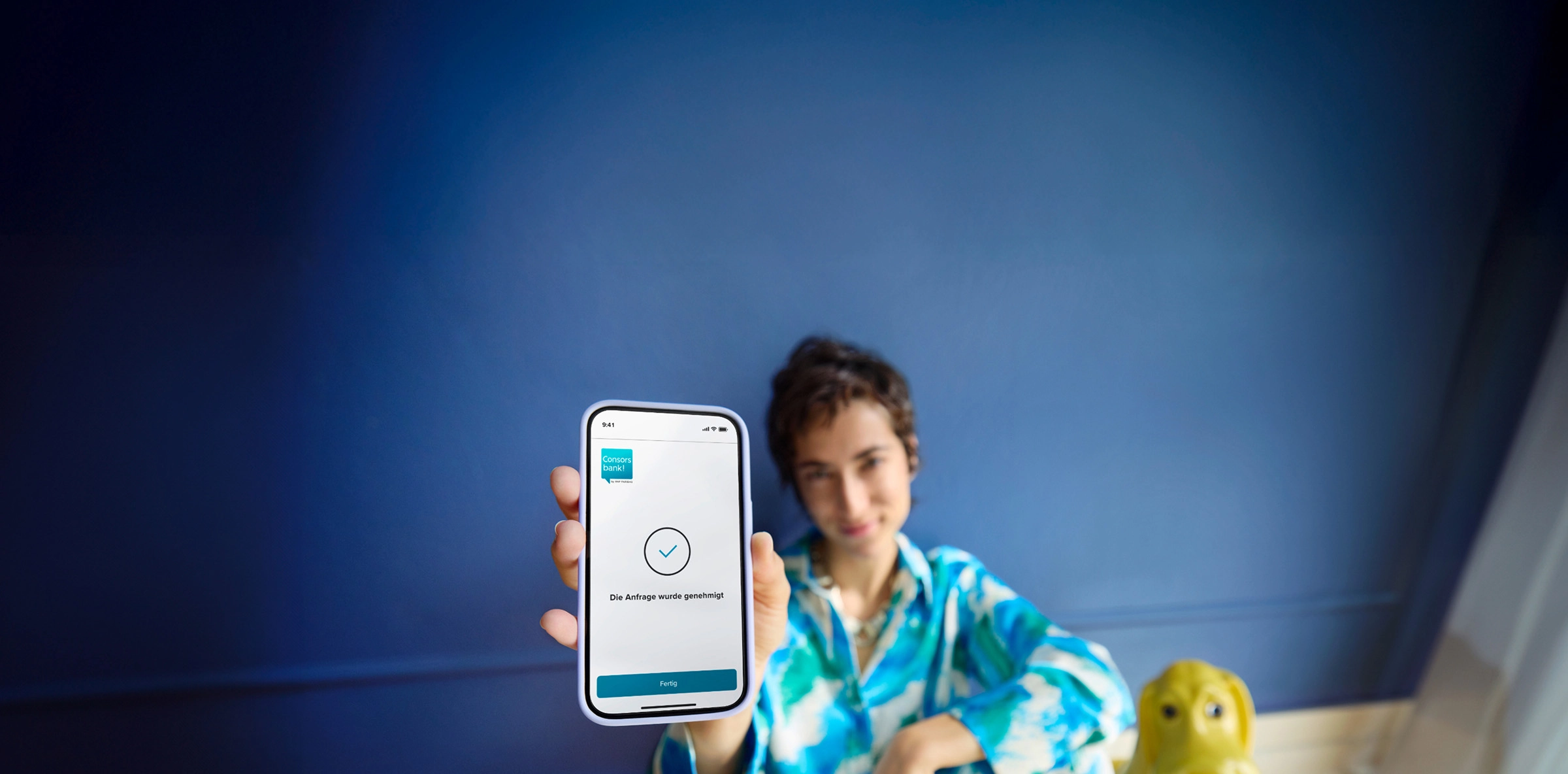 Frau vor blauer Wand sitzt am Boden und hält Smartphone in die Kamera