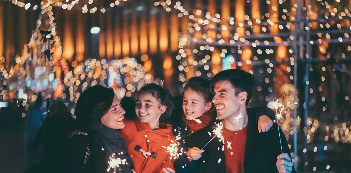 Familie mit zwei Kindern und Wunderkerzen. Im Hintergrund die Lichter eines Weihnachtsmarktes.