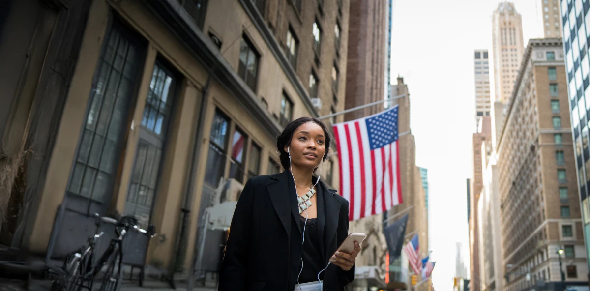 Frau steht auf offener Straße vor einem Gebäude mit USA-Flagge