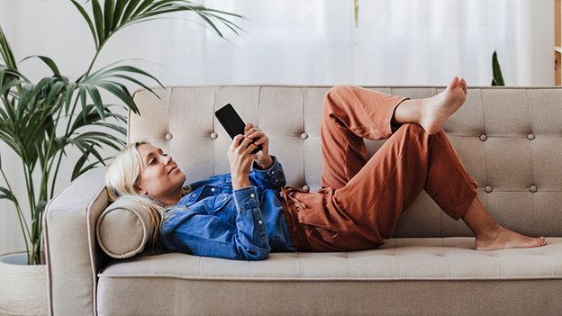 Frau auf dem Sofa liegend mit Smartphone in der Hand