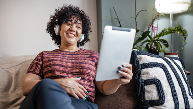 Lachende Frau auf dem Sofa am Tablet mit Kopfhörern