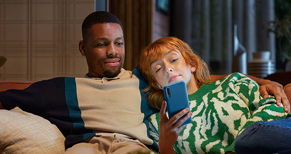 Mann und Frau sitzen auf Couch und schauen auf Smartphone
