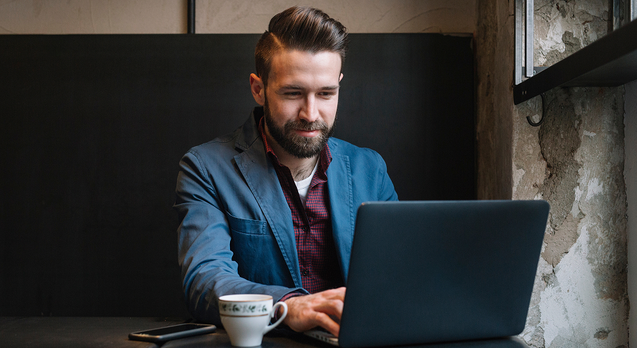 Mann in Hemd und blauen Sakko sitzt an seinem Laptop