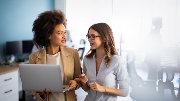 Zwei Frauen in Businessklamotten unterhalten sich an einem Laptop