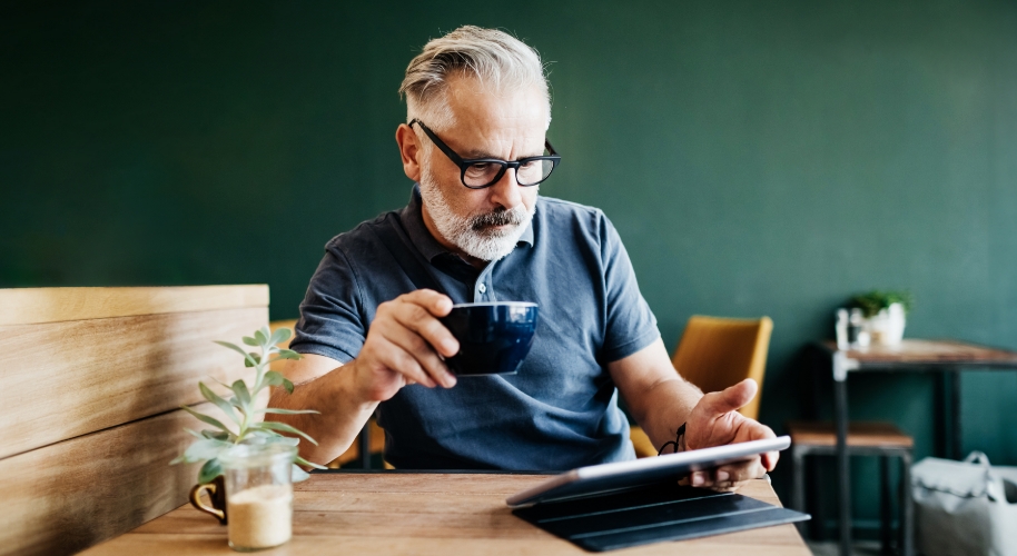 Mann mit Tasse in der Hand an Tablet